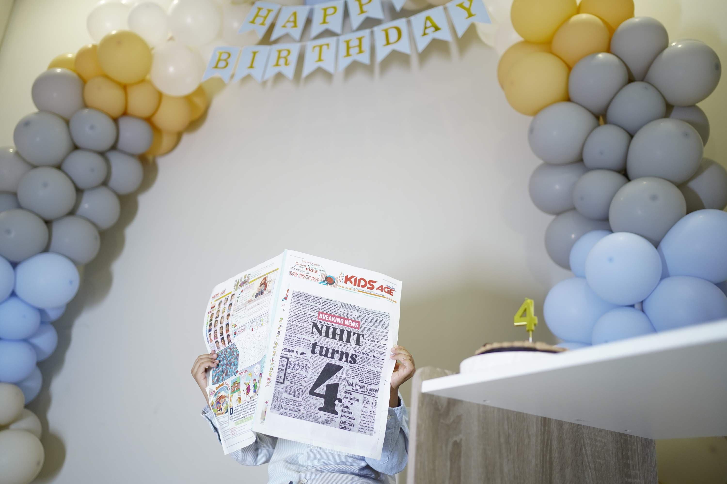 A boy holding his birthday newspaper under the balloon arch
