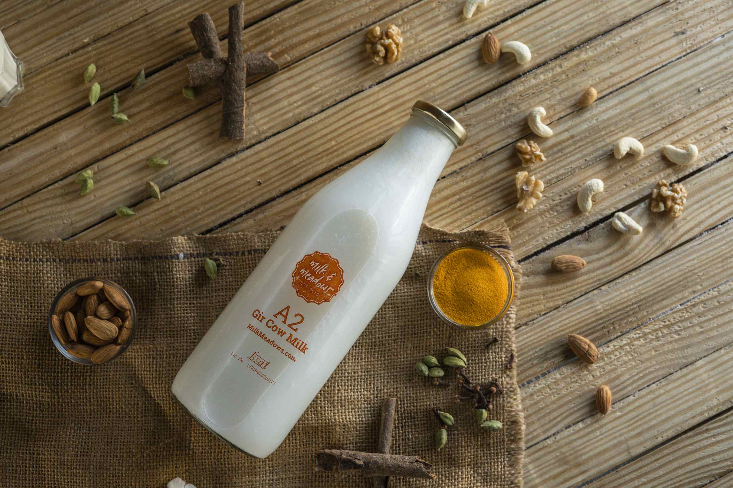 A2 milk bottle flat-lay with nuts, cardamom and saffron on jute