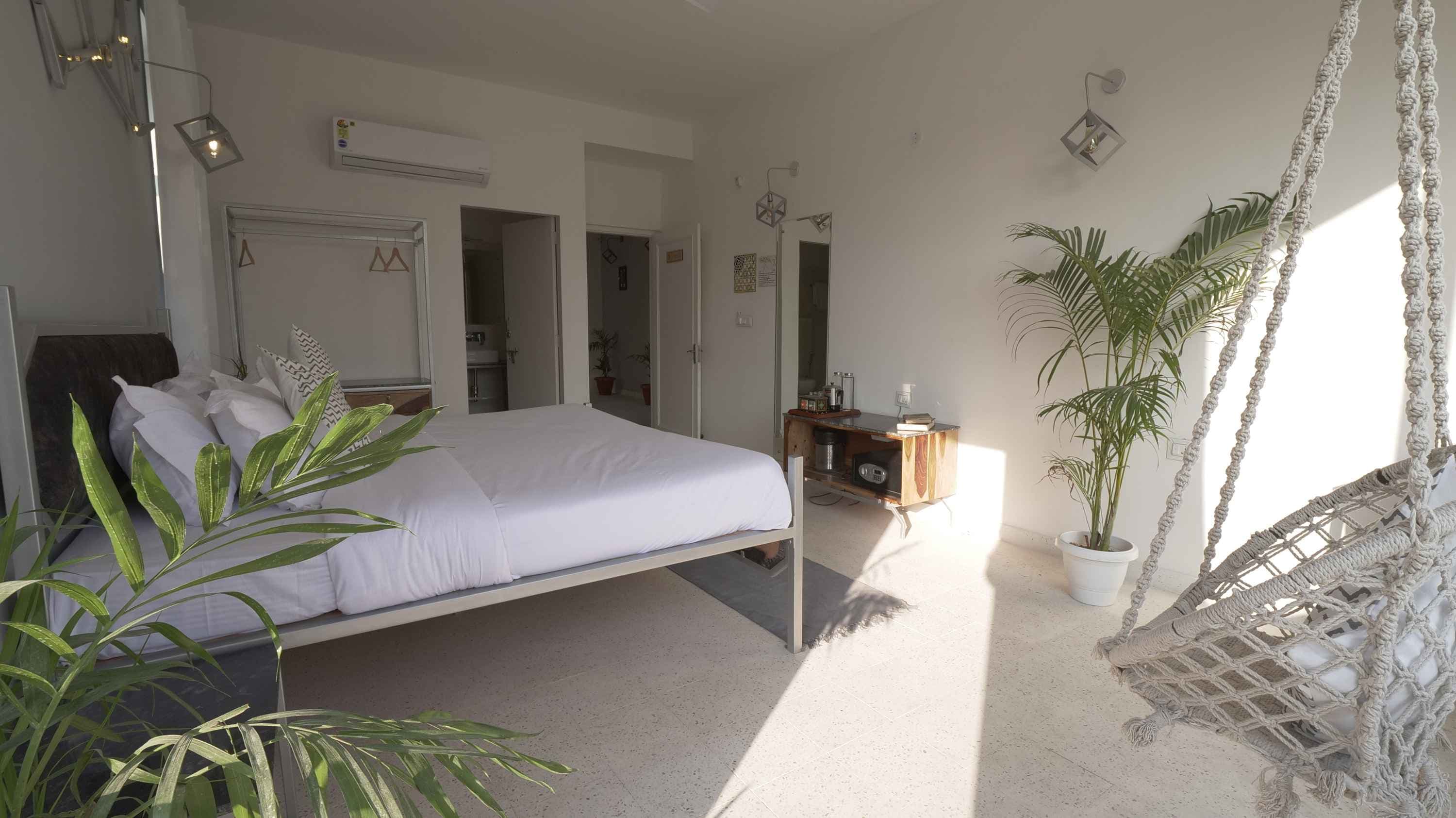 A white bedroom with a hanging swing chair and daylight through the blinds