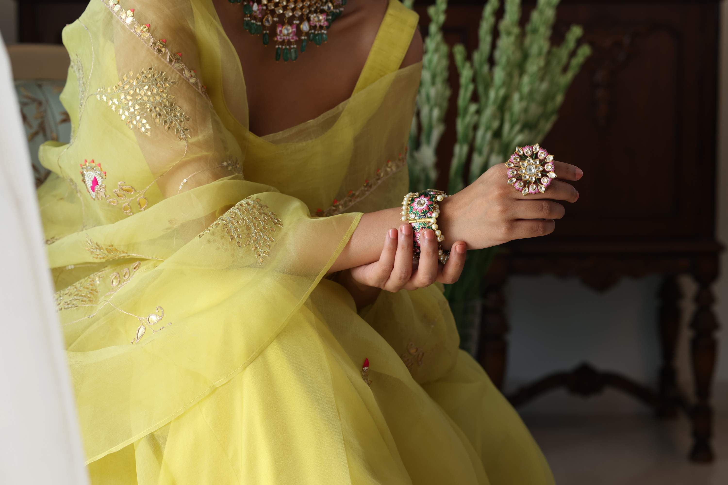 A yellow lehenga with the kundan ring and bangles, hands held out