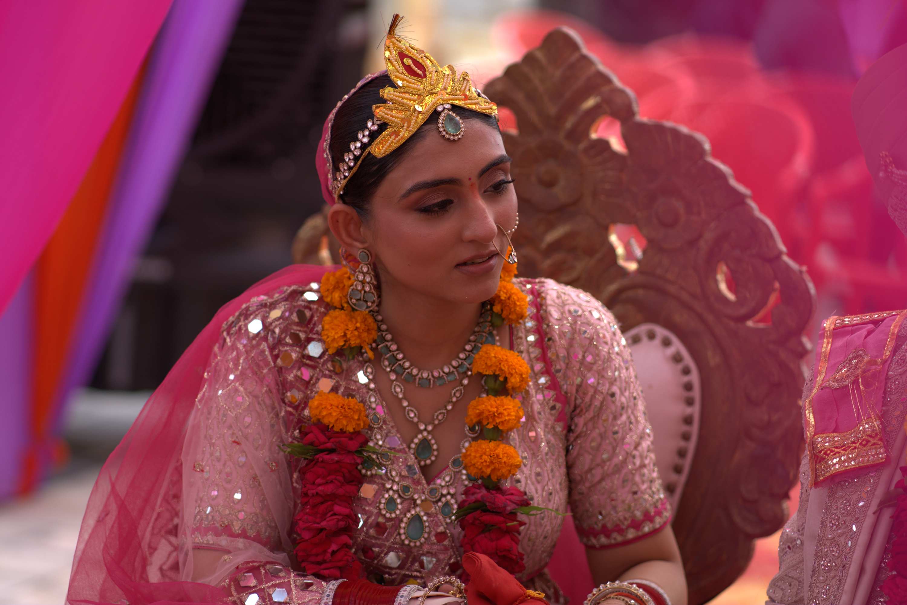 The bride in pink and a marigold garland, the mandap lit behind her