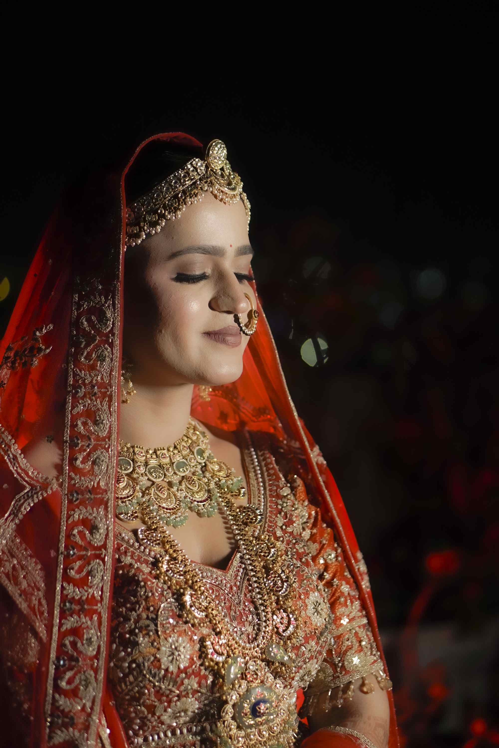 The bride in a red lehenga and gold jewellery, veil drawn back