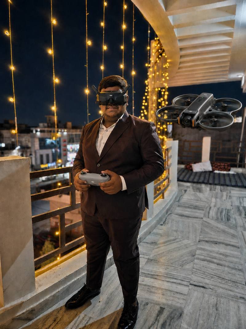 Krishna Bansal in FPV goggles, drone hovering beside him on a lit terrace