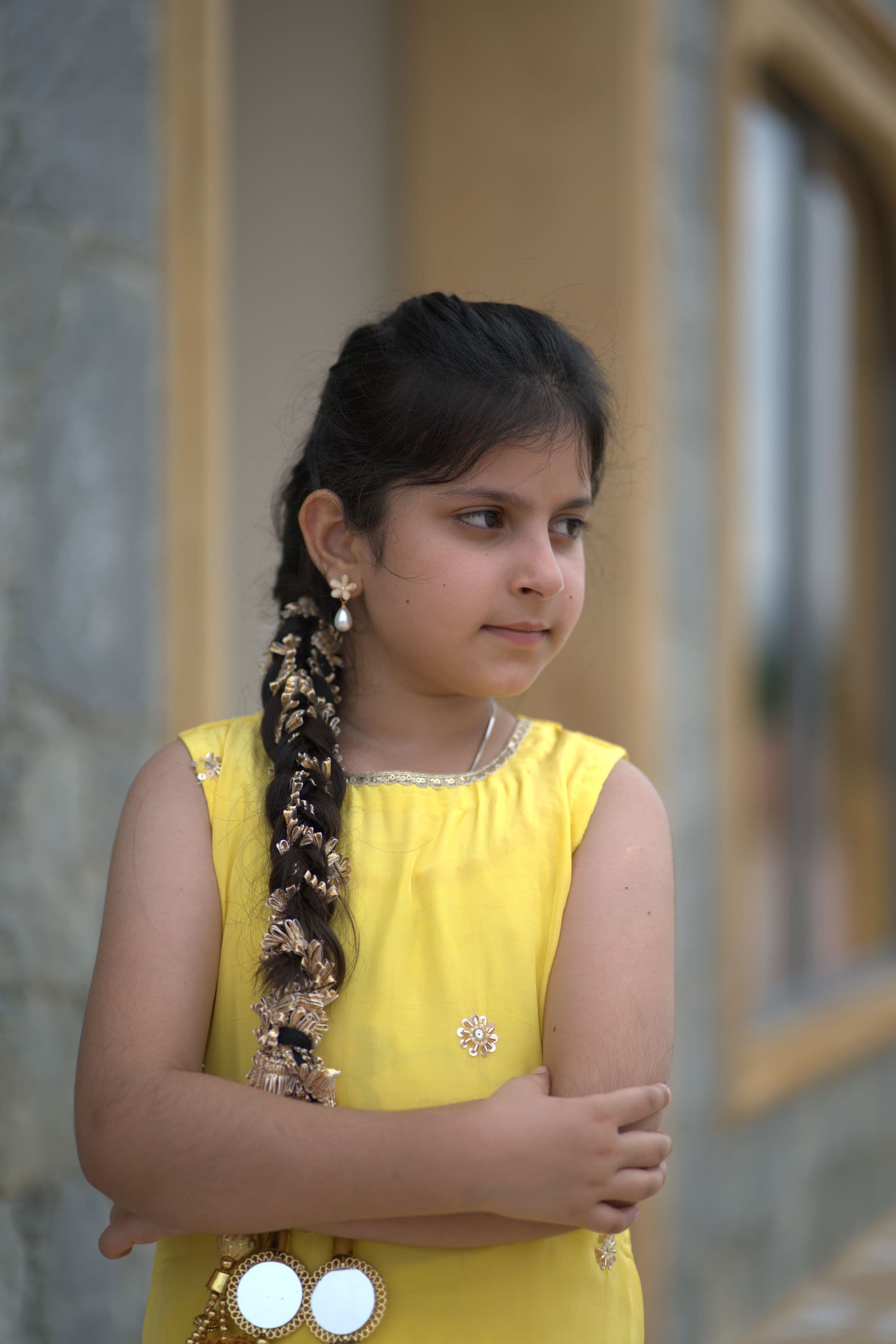 A girl in a yellow dress with a long braid, against a painted wall