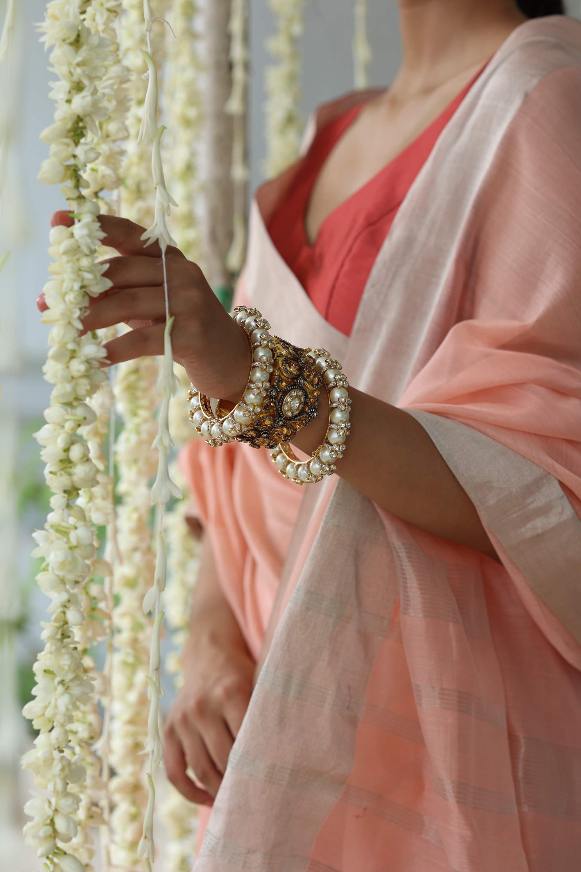 A hand in pearl bangles reaching through strings of jasmine