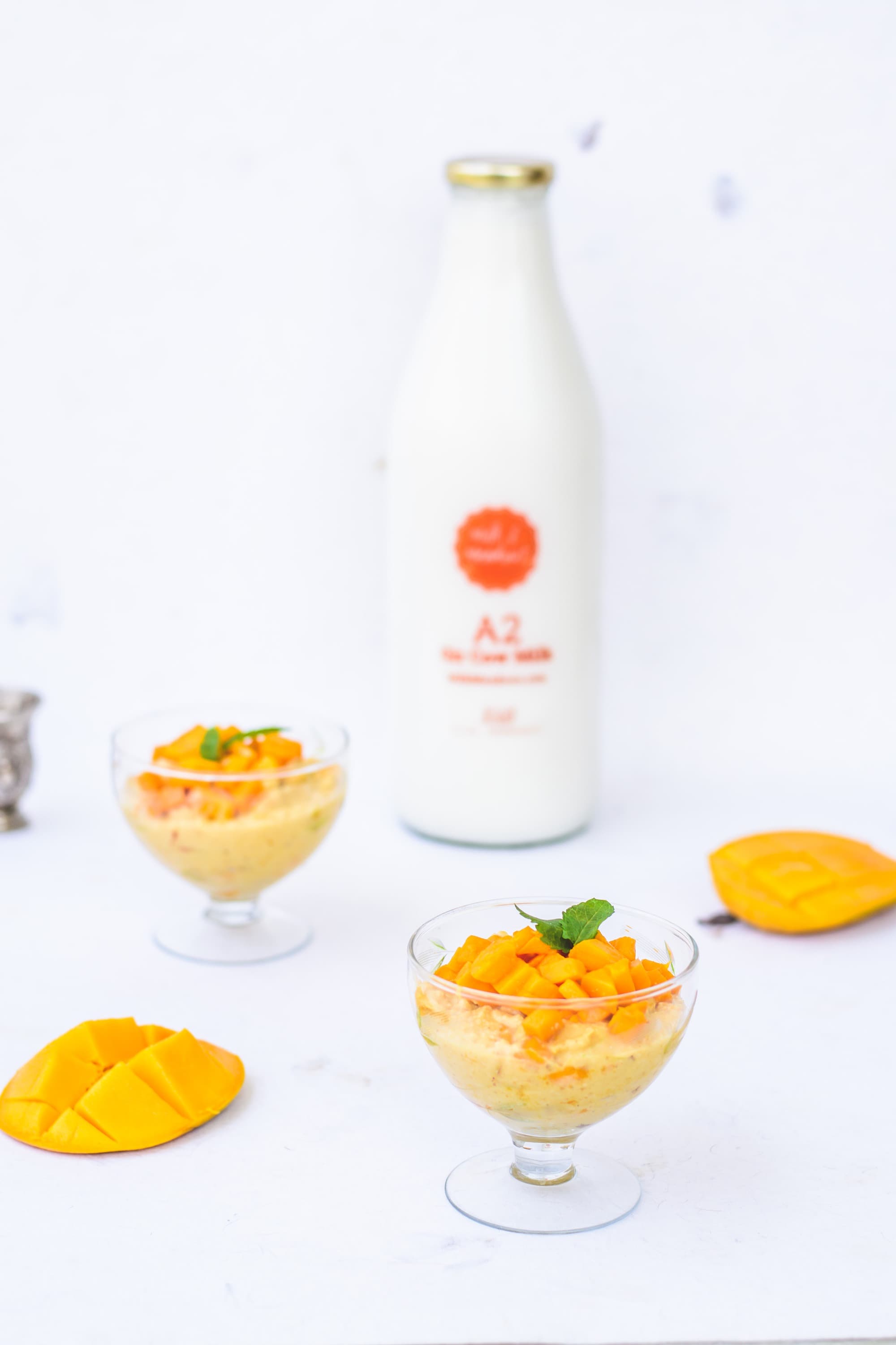 Mango shrikhand in two glass bowls with the milk bottle behind