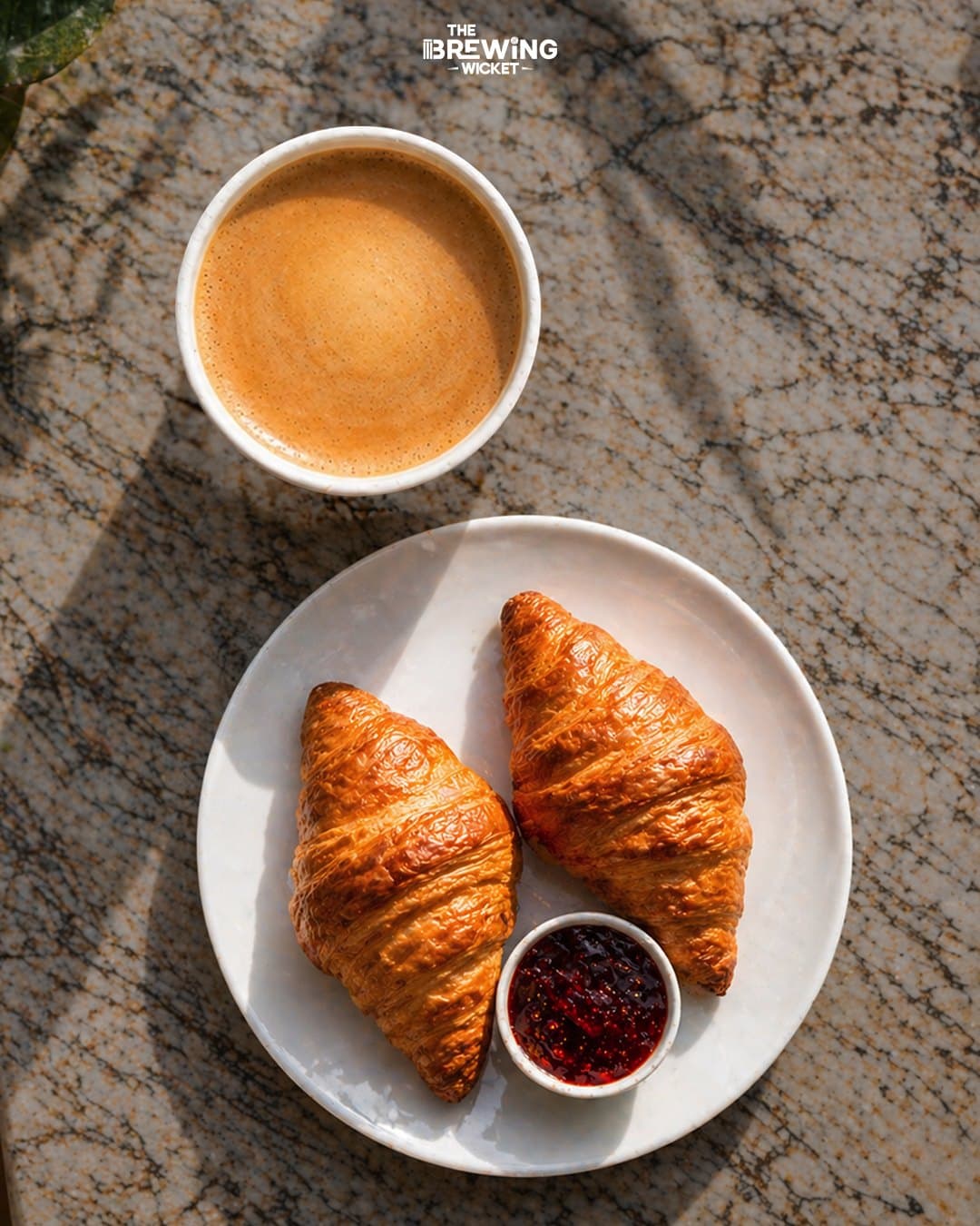 Flat-lay — coffee, two croissants and a pot of jam on marble